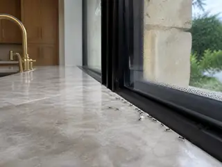 Tiny odorous house ants following a quartzite kitchen window seam toward a water droplet