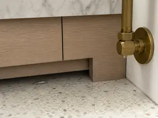 A silverfish beneath pale-oak laundry cabinetry near a plumbing supply line